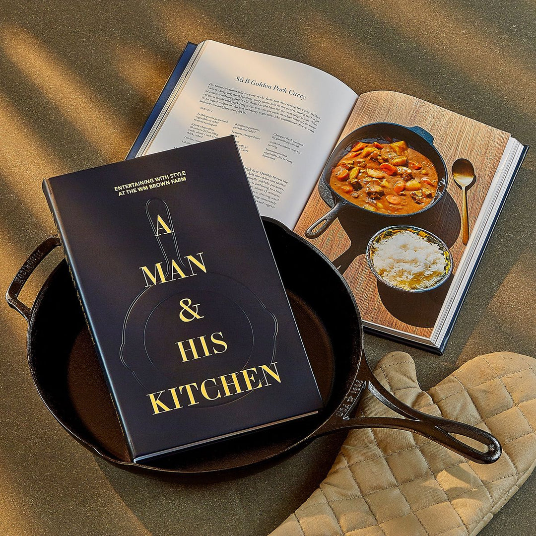 Cookbook titled 'A Man & His Kitchen' on a pan with a recipe book open showing a dish.