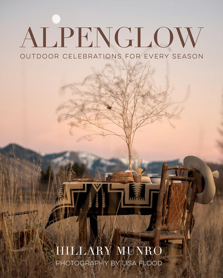 Book cover of 'Alpenglow' with a scenic outdoor setting, table, and chair.