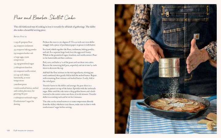Person seasoning food in a skillet with a sifter, next to a recipe on a wooden surface.
