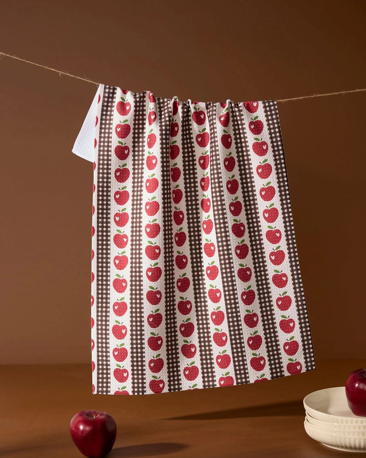 Dish towel with red apple pattern hanging on a line against a brown background
