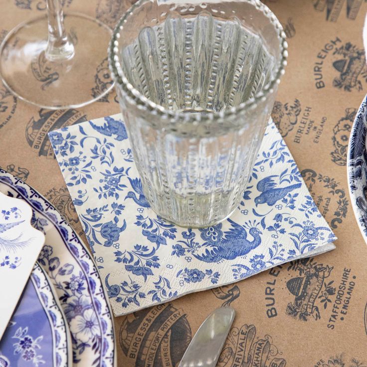 Clear glass on a blue and white patterned napkin with a brown paper background featuring branding.