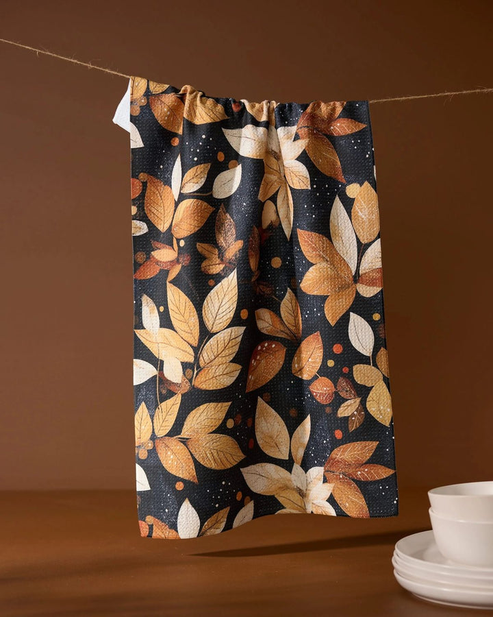 Tea towel with autumn leaf pattern hanging on a line against a brown background
