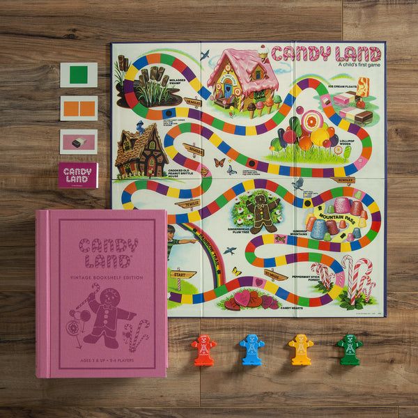 Candy Land board game set with colorful board, pink book, and toy figures on a wooden surface