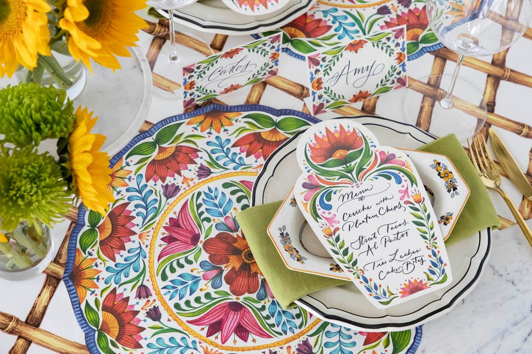 Colorful table setting with floral plates and place cards on a wooden table.