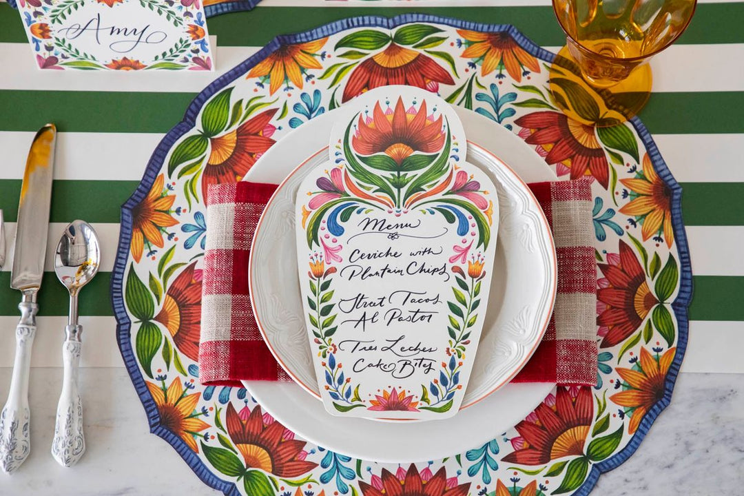 Colorful table setting with floral plates and a menu card on a striped tablecloth.
