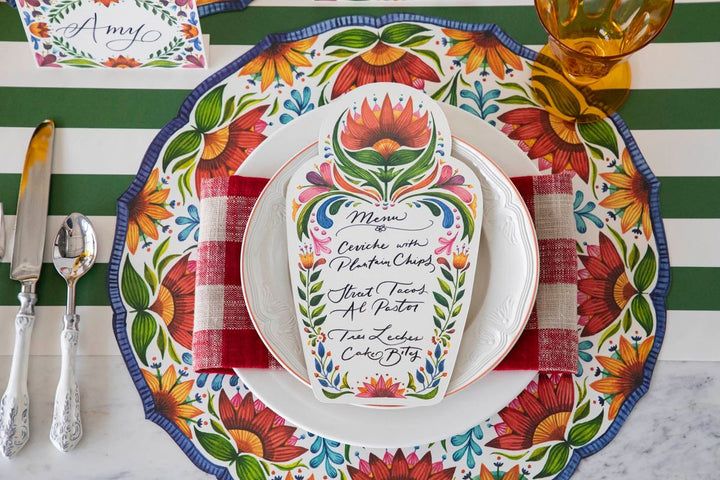 Colorful table setting with floral plates and a menu card on a striped tablecloth.