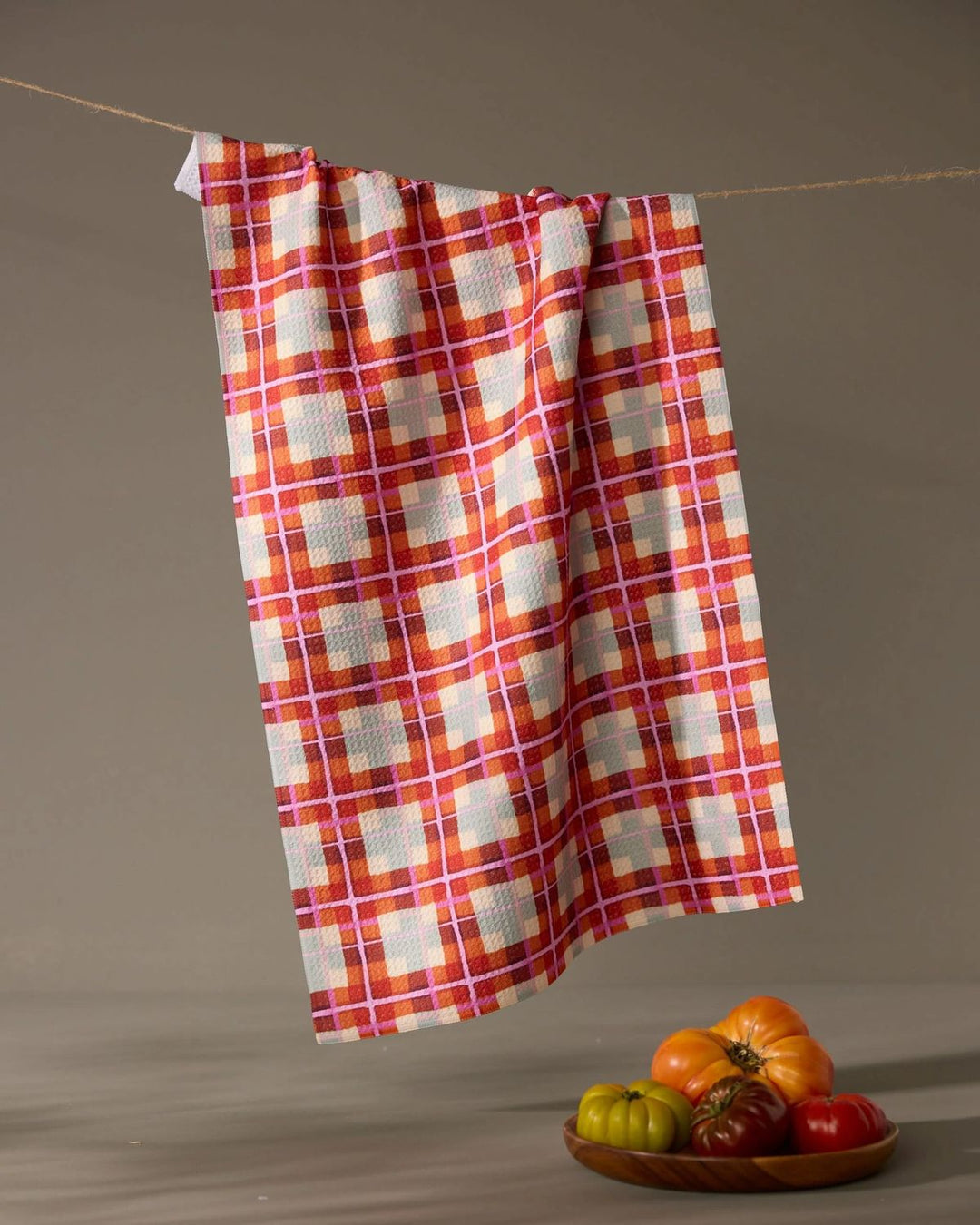 Plaid towel hanging on a line with a plate of vegetables below against a neutral background