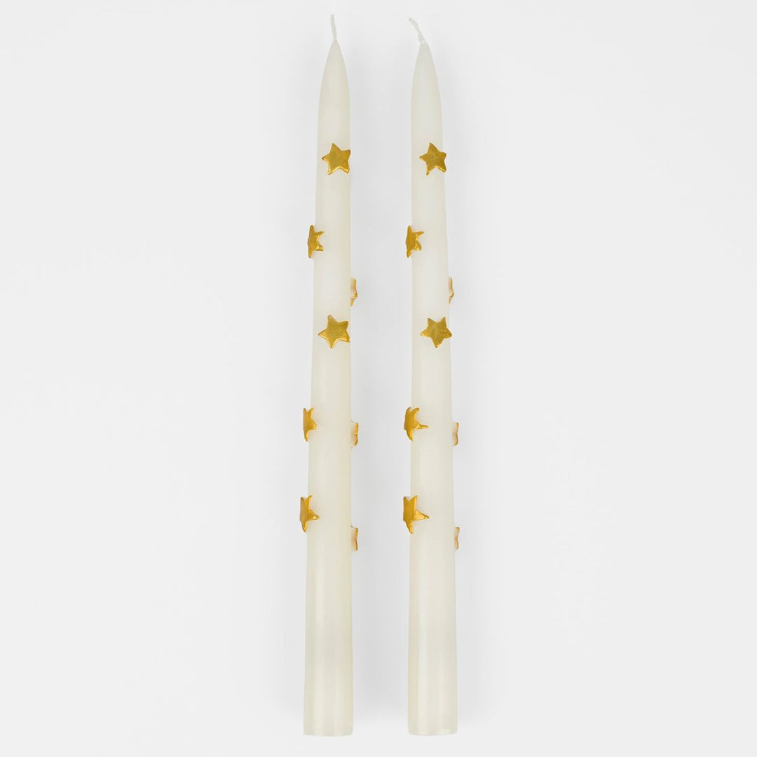 Two white candles with gold star patterns on a white background
