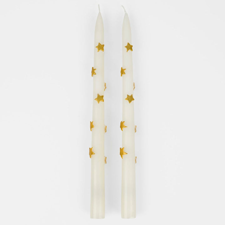 Two white candles with gold star patterns on a white background