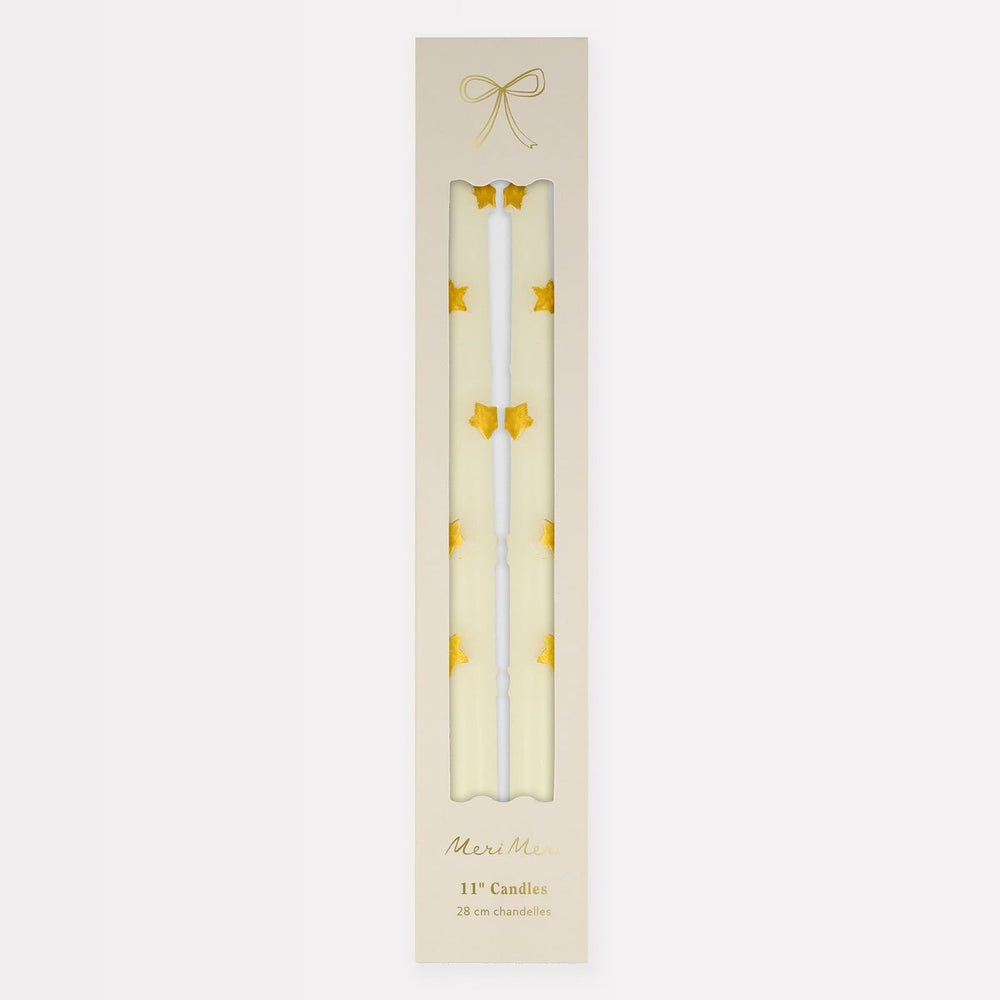 Two white candles with gold stars in a decorative box on a light beige background