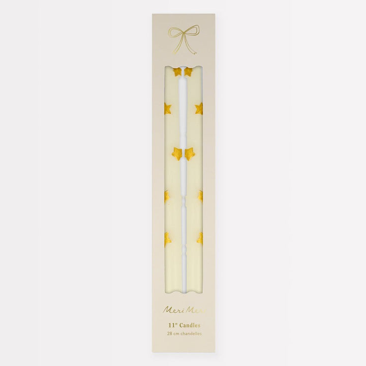 Two white candles with gold stars in a decorative box on a light beige background