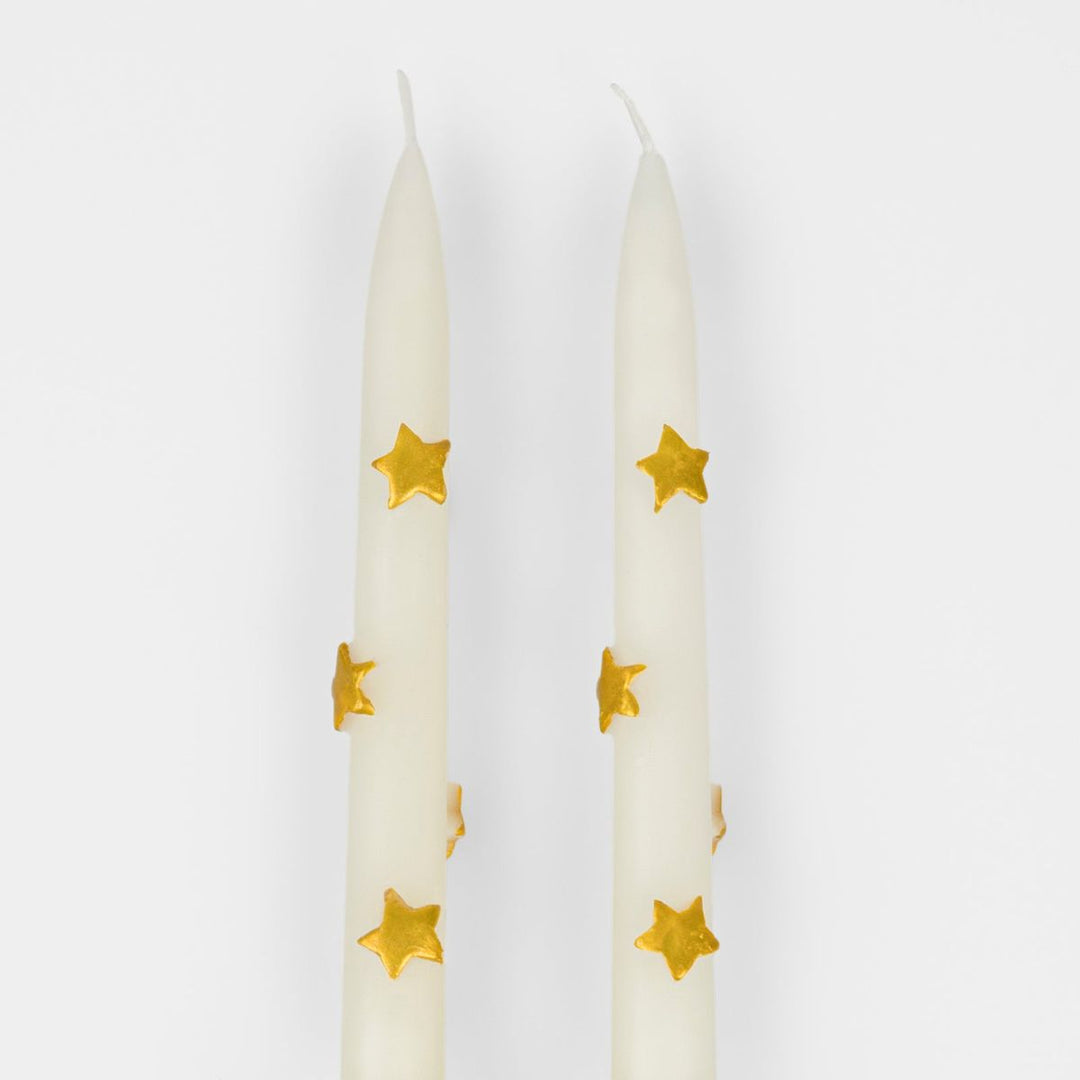 Two white candles with gold star patterns on a white background