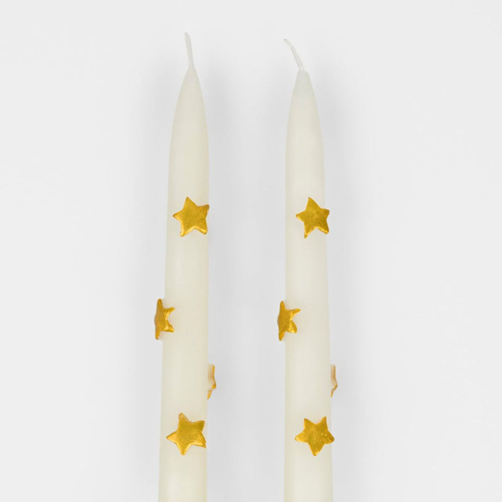 Two white candles with gold star patterns on a white background