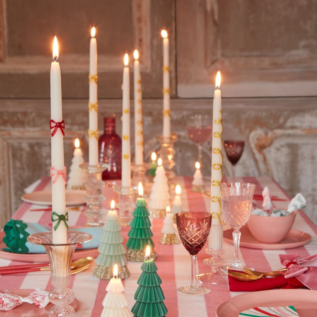 Decorative candles and table settings on a festive tablecloth with a fireplace in the background.