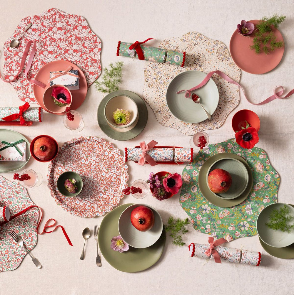 Decorative table setting with floral placemats, pomegranates, and crackers on a light background
