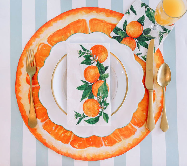 Table setting with orange-themed plates, cutlery, and placemats on a striped tablecloth.
