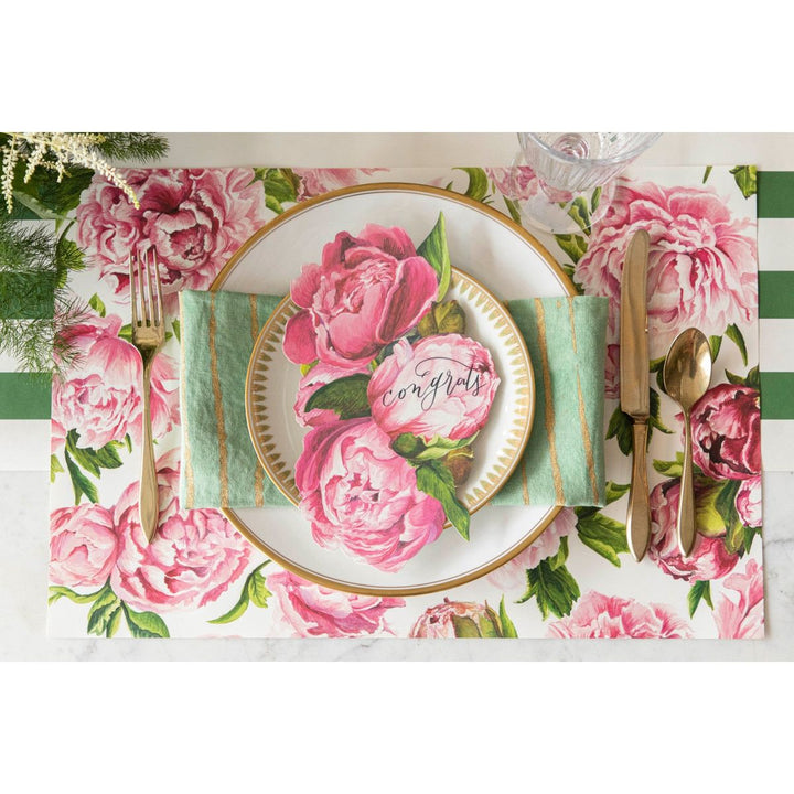 Table setting with floral placemat, plate, and cutlery on a checkered tablecloth.
