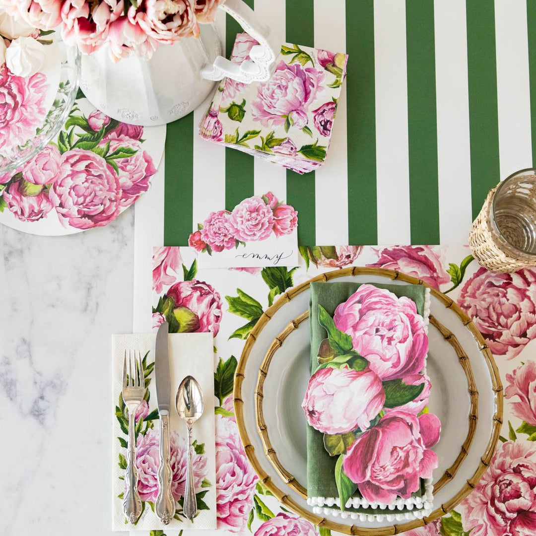 Table setting with floral tablecloth, napkins, and cutlery on a green and white striped background.