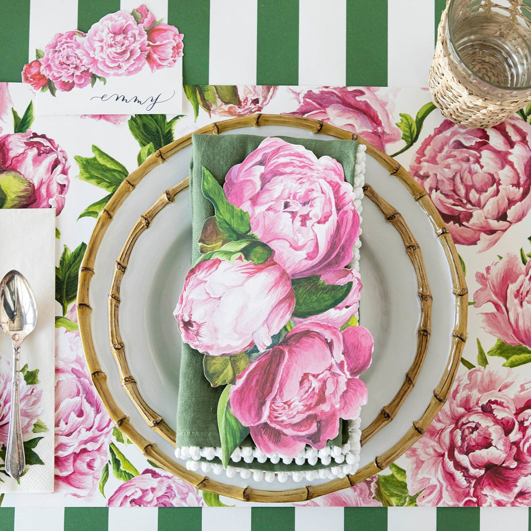 Floral table setting with pink peony napkin on a green and white striped tablecloth.