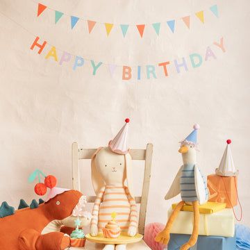 Children's birthday party setup with stuffed animals wearing party hats and a 'Happy Birthday' banner.