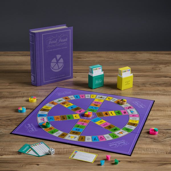 Board game setup with a purple board, dice, and cards on a wooden surface.