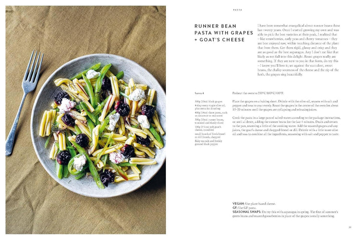 Plate of runner bean pasta with grapes and goat's cheese on a brown surface, next to a fork.