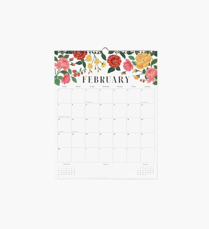 A hanging monthly calendar page for February with a colorful floral border at the top and a clean white grid layout below.