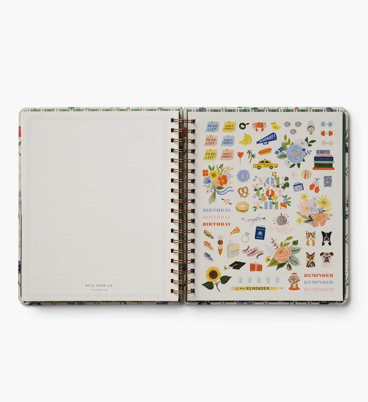 An open spiral-bound planner or notebook showing a decorated sticker sheet on the right page with colorful birthday-themed illustrations, set against a clean white background.