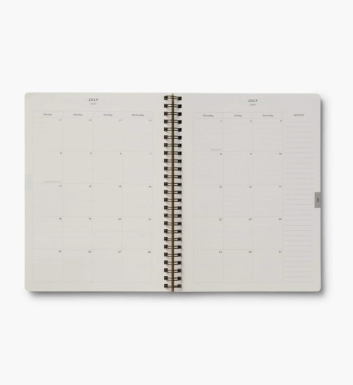 An open spiral-bound planner or calendar showing the month of July with daily and weekly layout pages on a light gray background.