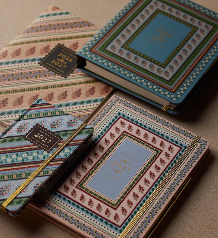 Decorative notebooks with intricate patterns and gold accents on a beige surface