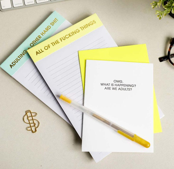 Four notepads with humorous text on a desk with a pen and paper clip.