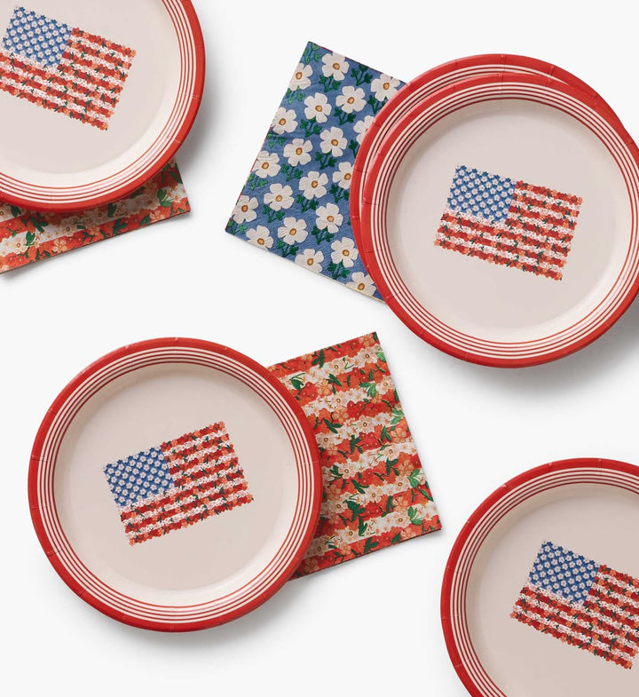Ceramic plates with American flag design on a white surface with floral and patterned napkins.