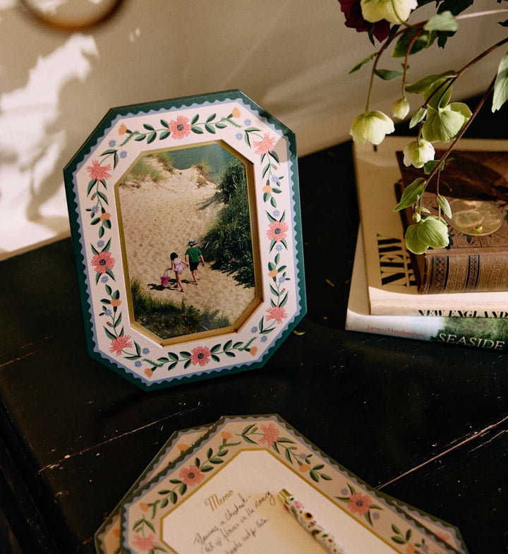 Decorative photo frame with floral design on a surface with books and plants.