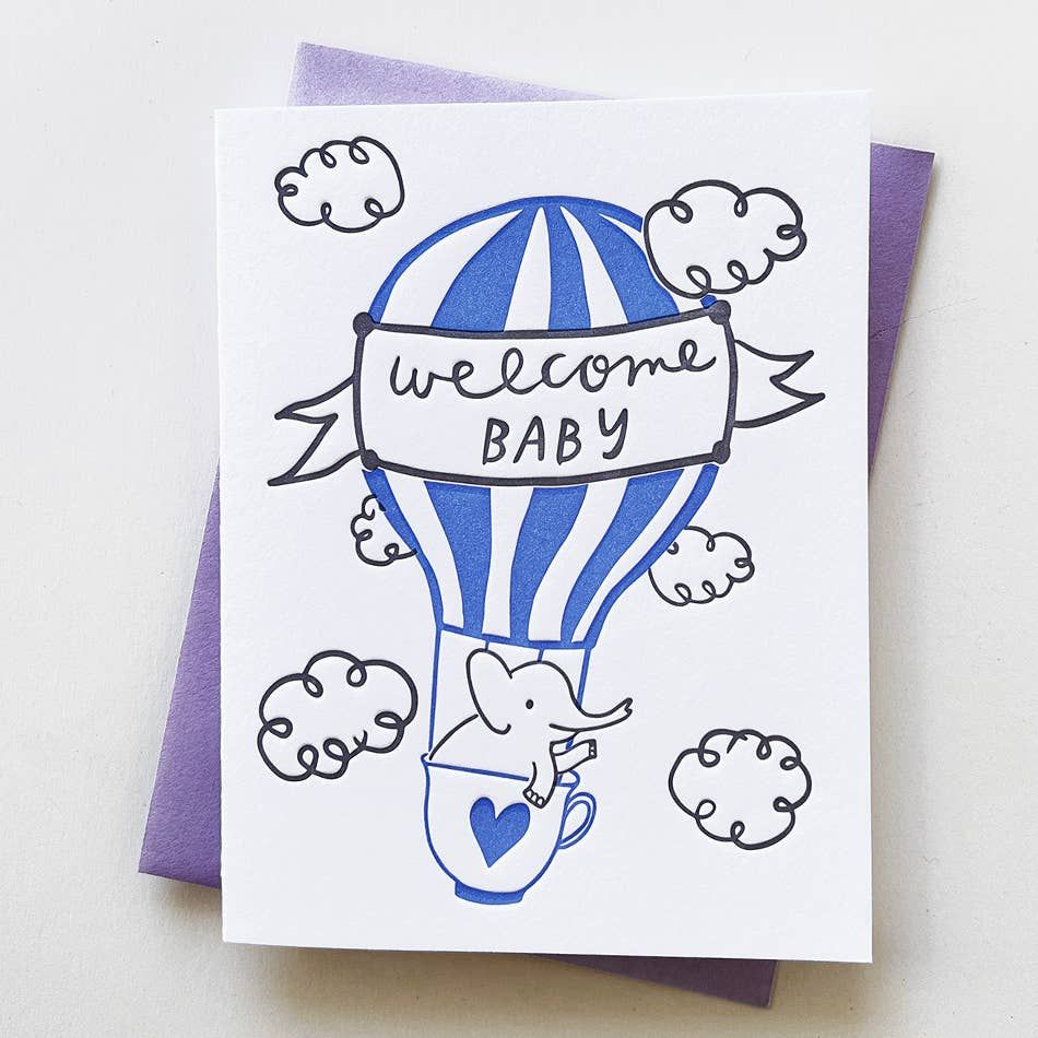 Greeting card with a blue hot air balloon and 'welcome baby' banner on a white background.