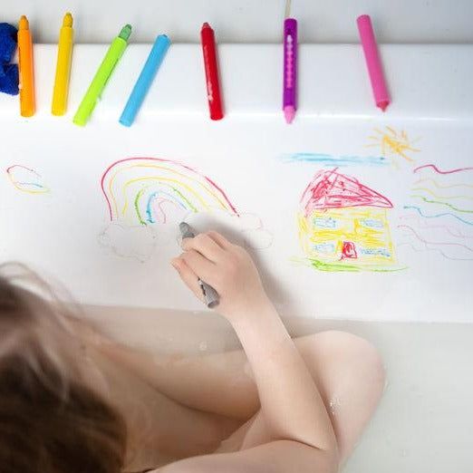 Child drawing with colorful crayons on a white surface