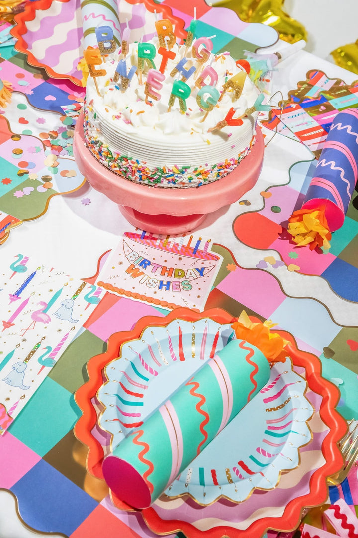 Colorful birthday-themed table setting with cake, plates, and decorations.