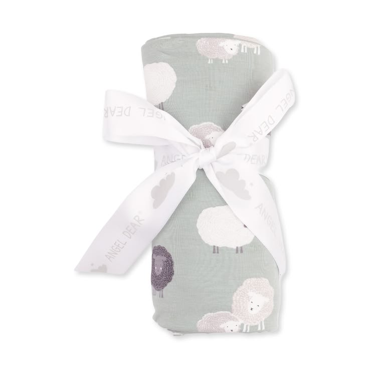 A rolled baby swaddle blanket with a sheep pattern in sage green, white, and lavender, tied with a white ribbon printed with the brand name 'Angel Dear'.