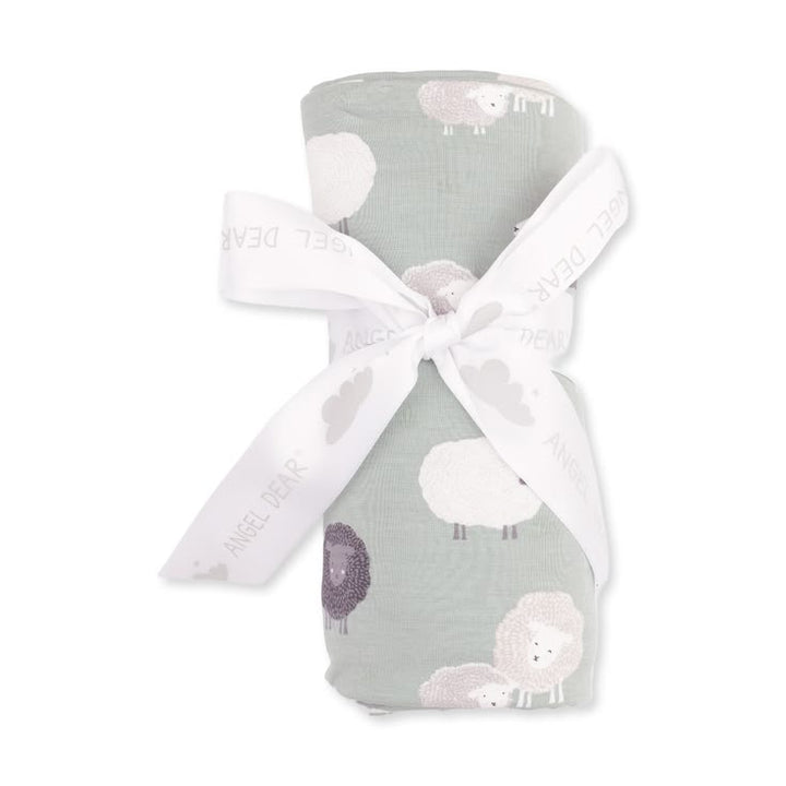 A rolled baby swaddle blanket with a sheep pattern in sage green, white, and lavender, tied with a white ribbon printed with the brand name 'Angel Dear'.