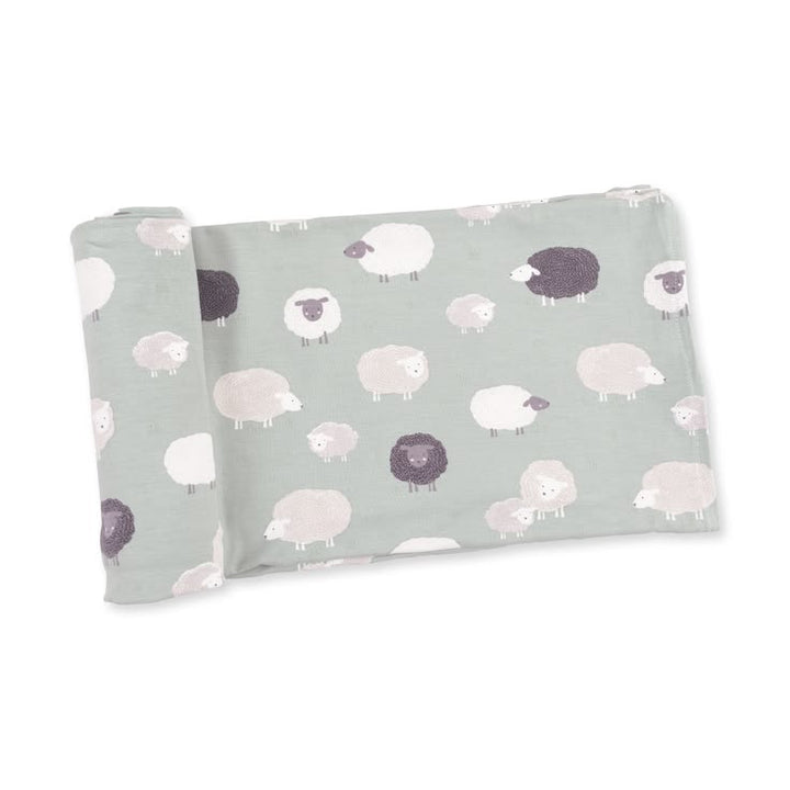 A folded baby blanket or swaddle with a repeating pattern of cute sheep in white, light gray, and dark charcoal on a muted sage green background, shown on a clean white studio background.
