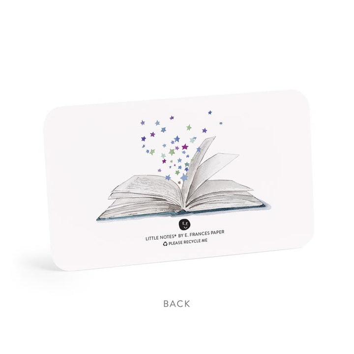 The back of a white card or packaging insert featuring an illustration of an open book with colorful stars rising from it. Text on the card reads 'LITTLE NOTES BY E.