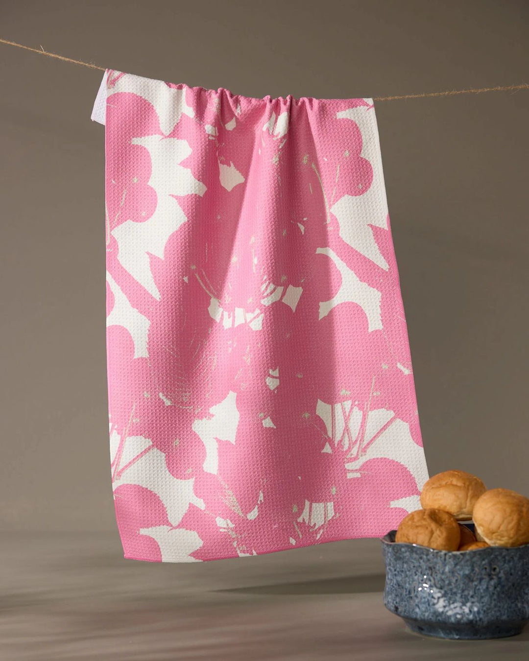 Pink and white patterned towel hanging on a line with a bowl of bread below.