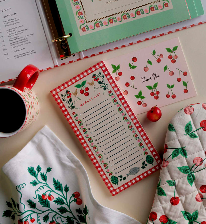 Cherry-themed kitchen items including a mug, notepad, and pot holder on a table.