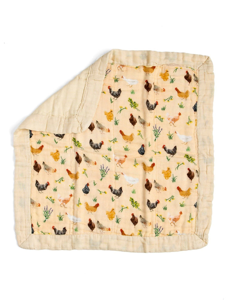 A square muslin baby blanket with a chicken and grass pattern on a light beige background, featuring a solid beige border and a folded corner showing the reverse side.