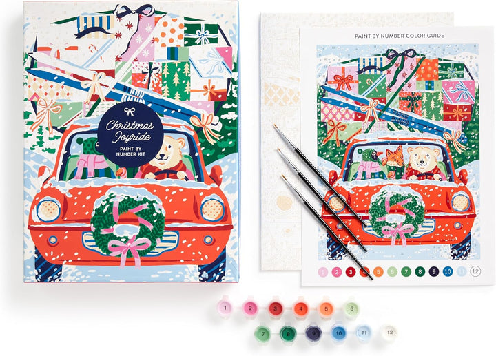 Christmas-themed paint-by-number kit shown with its illustrated box, color guide sheet, paintbrushes, and small paint tubes on a white background.