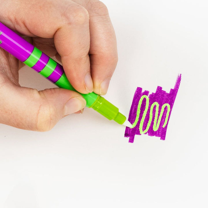 Hand holding a green and purple marker with a sample of purple line on a white background