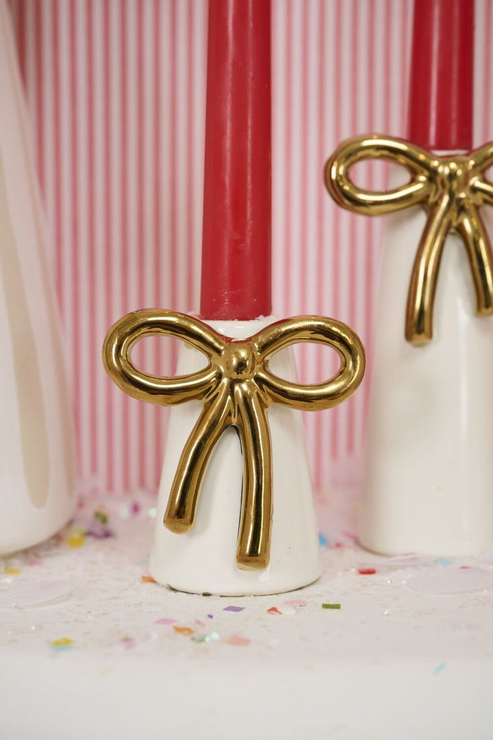 Decorative items with gold bows on white bases against a striped background