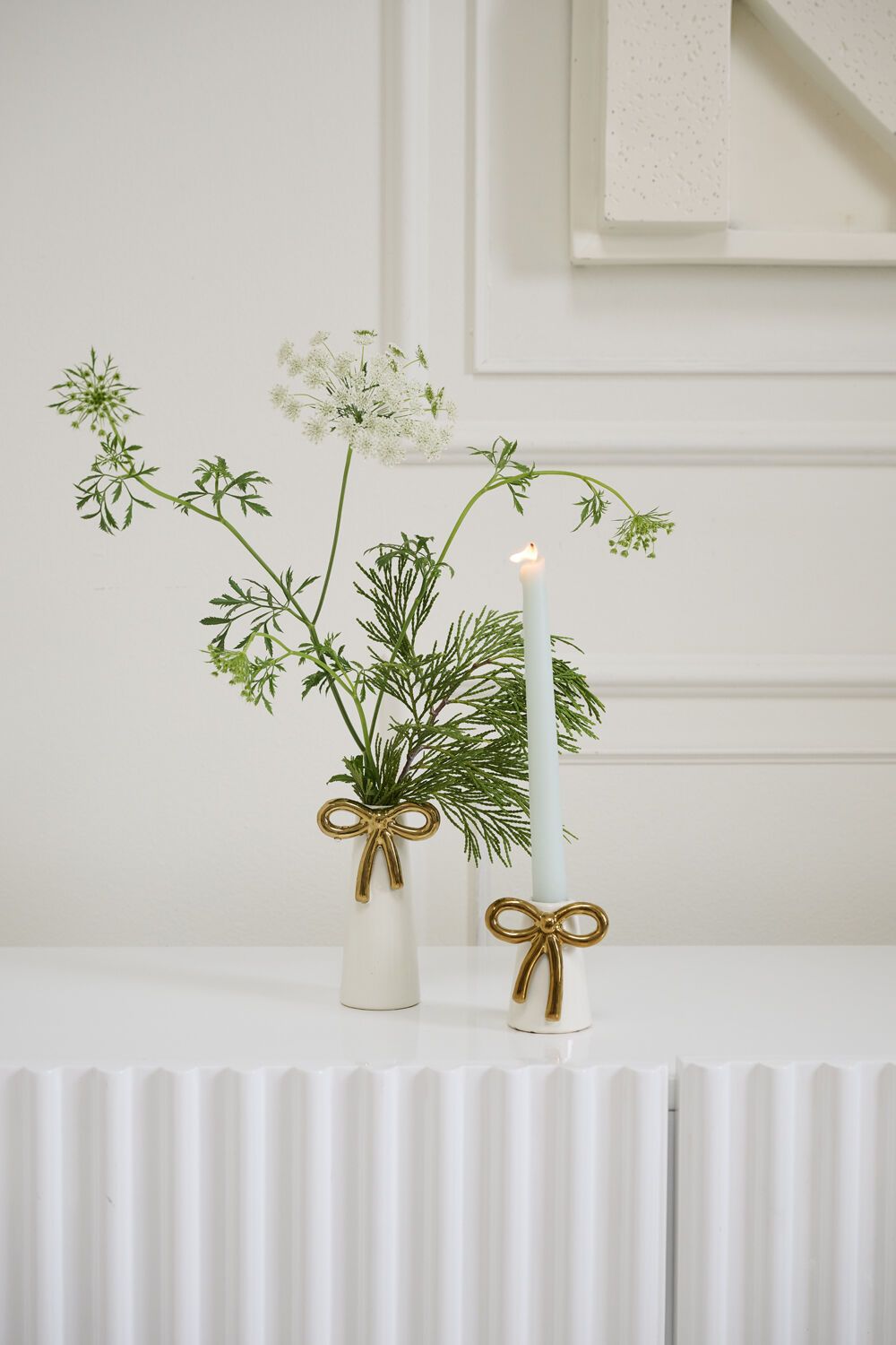 Vase with greenery and a candle on a white surface with a neutral background