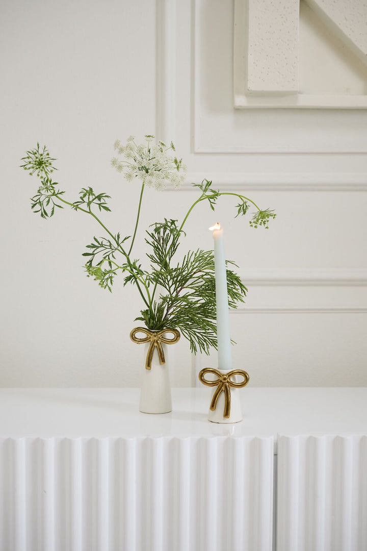 Vase with greenery and a candle on a white surface with a neutral background