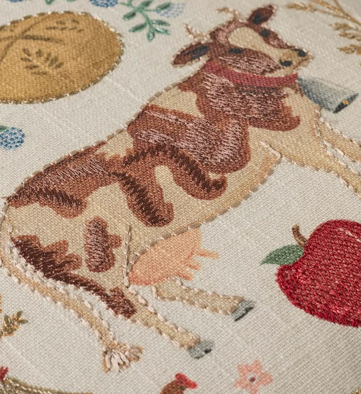 Embroidered design of a deer with flowers and an apple on a beige background