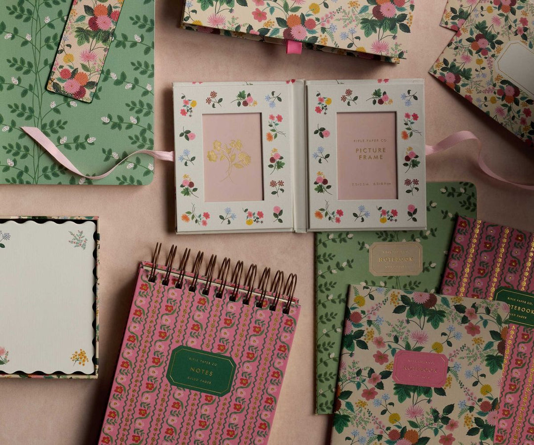 Collection of floral-themed stationery items on a pink surface
